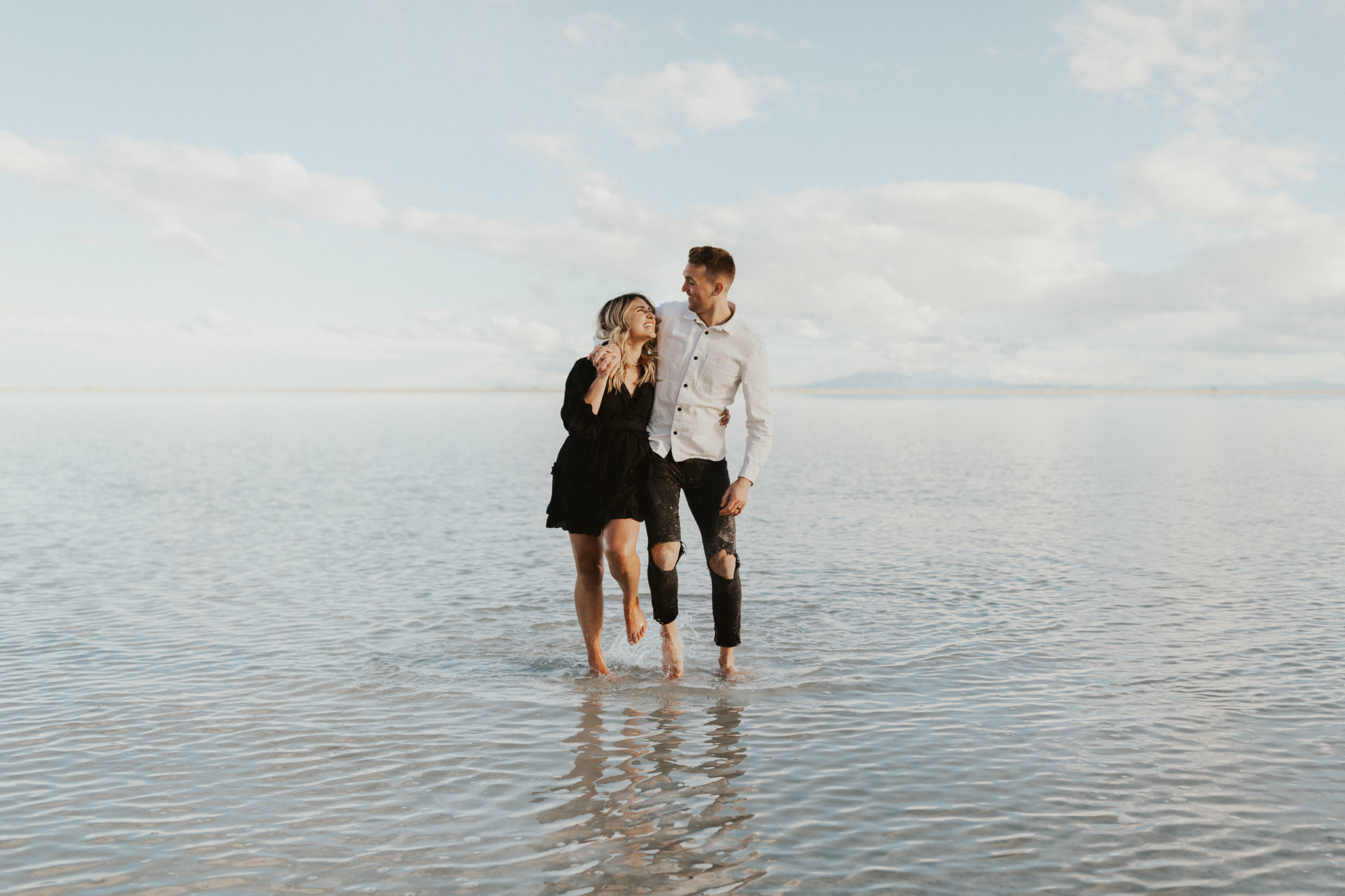 Couple dressed in neutral colors, walking in water during engagement session